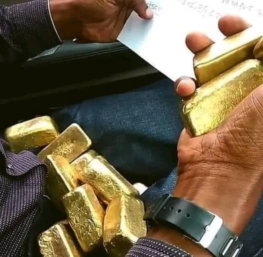 Cast gold bullion bars held in hand alongside a paper document listing their details
